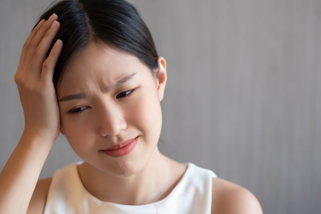めまいで頭をおさえる女性